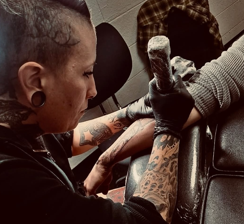 Hannah Arthur tattooing a client's arm with black and grey detail work